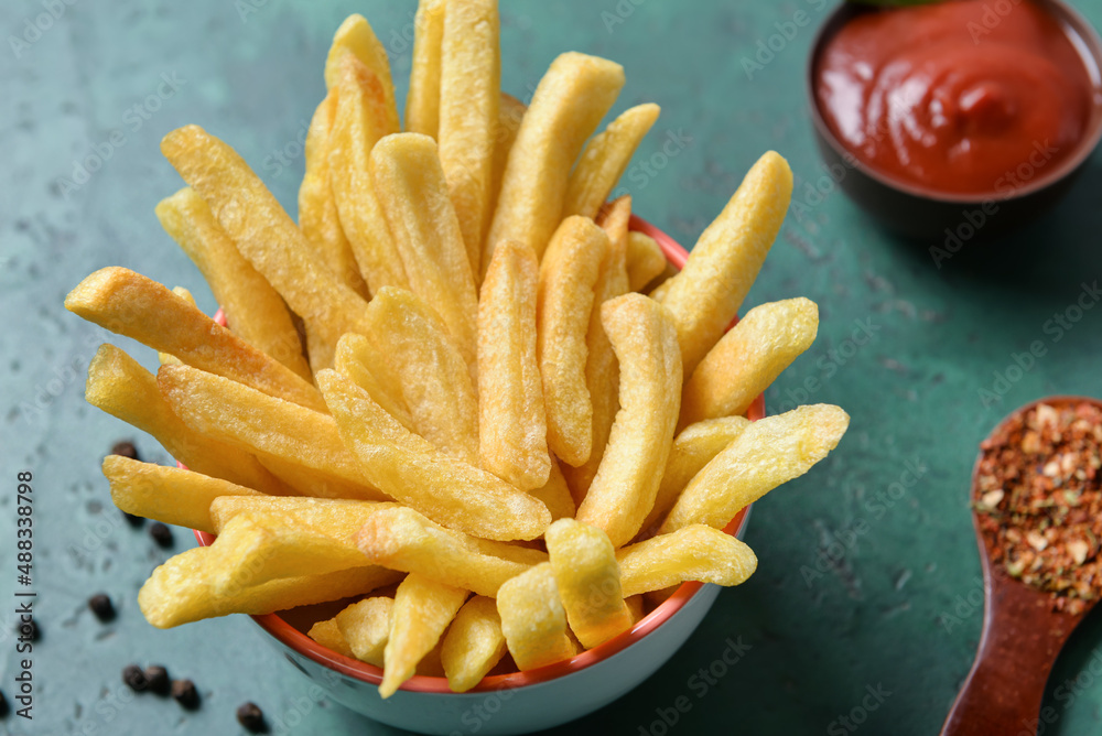 Bowl with tasty french fries on green background