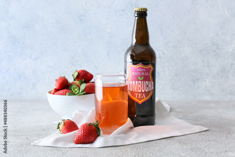 Bottle and glass of fresh strawberry kombucha on light background