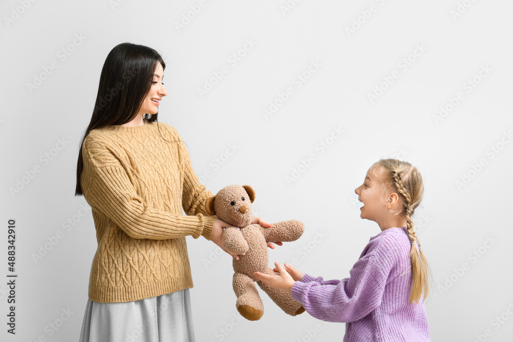 Happy mother giving toy to her little daughter on light background