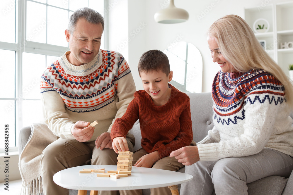 Little boy with his grandparents in warm sweaters playing jenga game at home