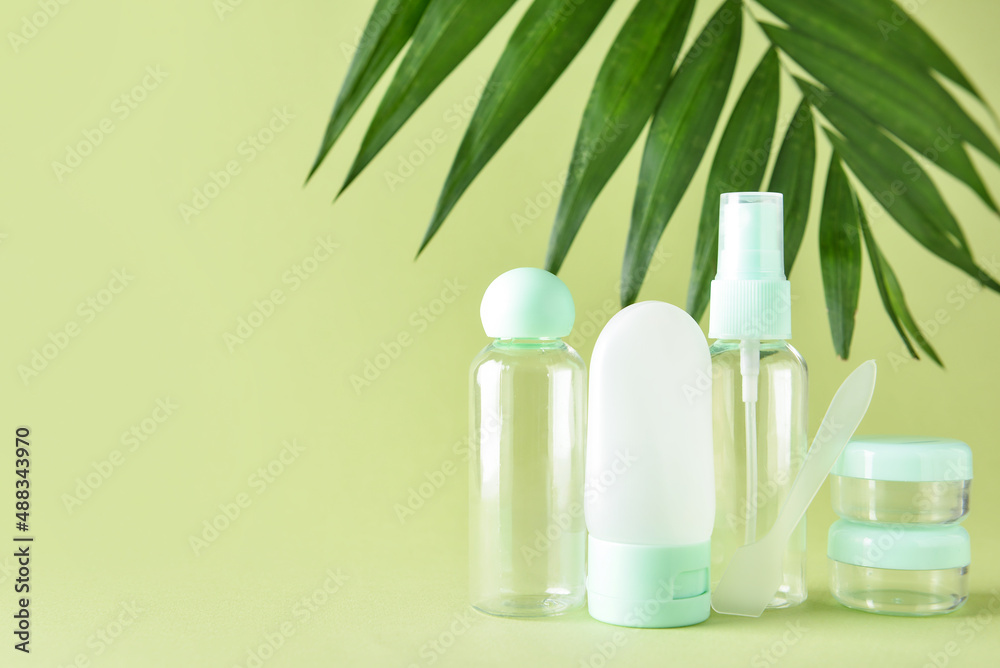 Set of travel bottles, jars and palm leaf on green background