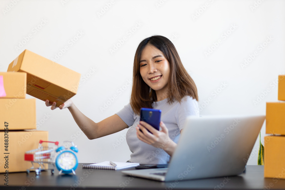 Young Asian woman starting a small e-commerce business working on laptop internet and talking to cus