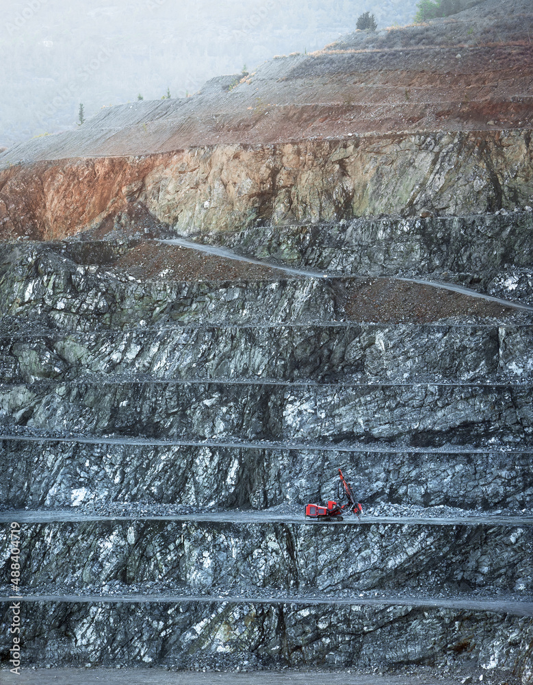 Red drilling machine on a bench of diabase quarry in misty morning