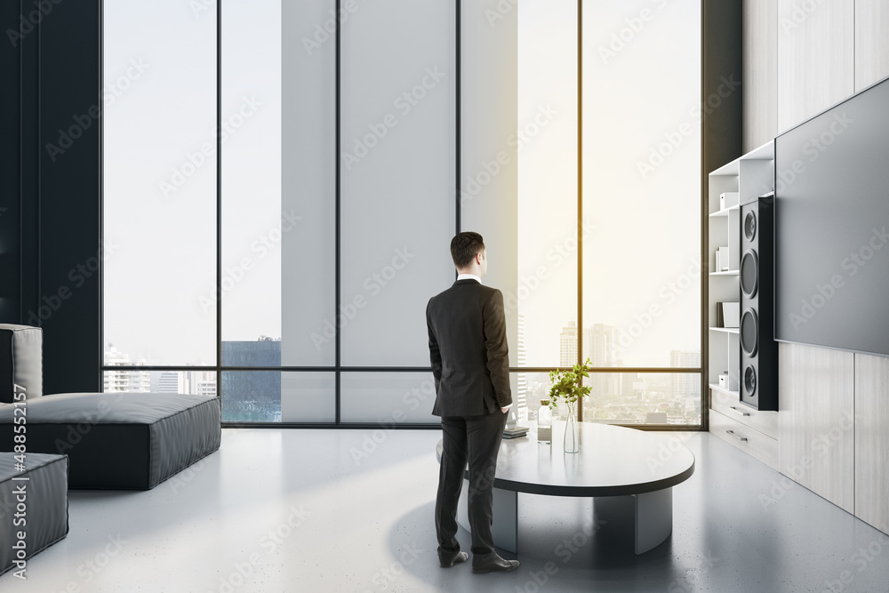 Young european businessman looking out of window in modern office room interior. Future, tomorrow an