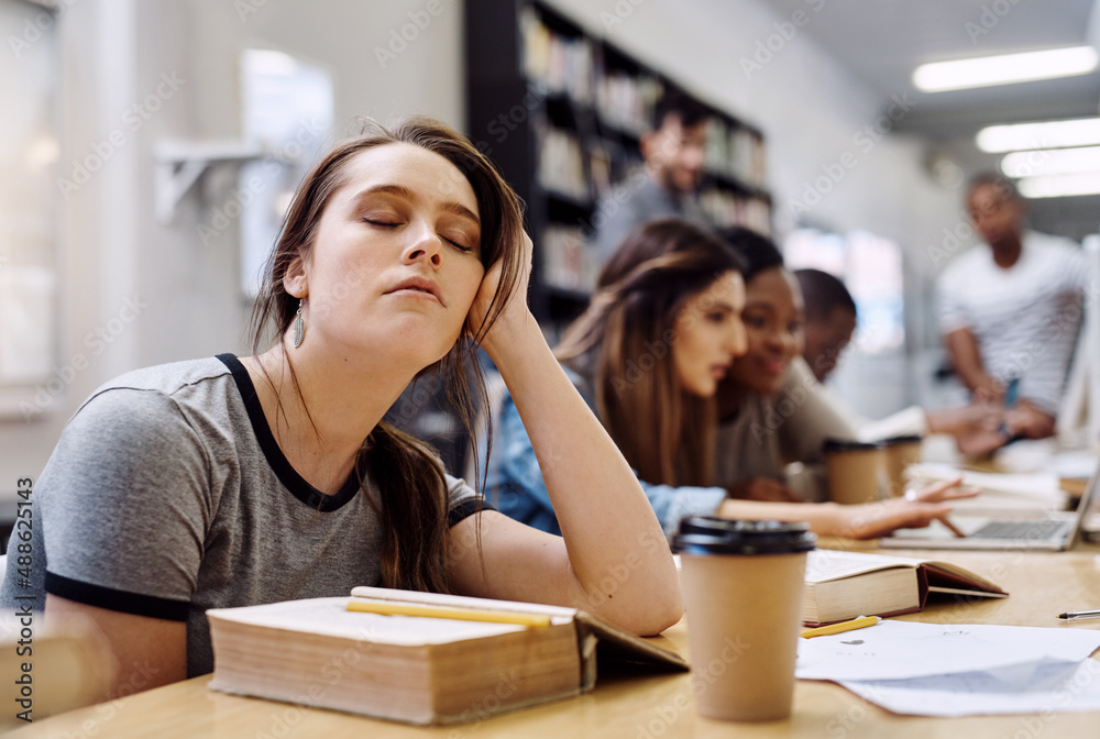 Im just closing my eyes for a bit. Shot of a young woman looking tired while studying in a college l