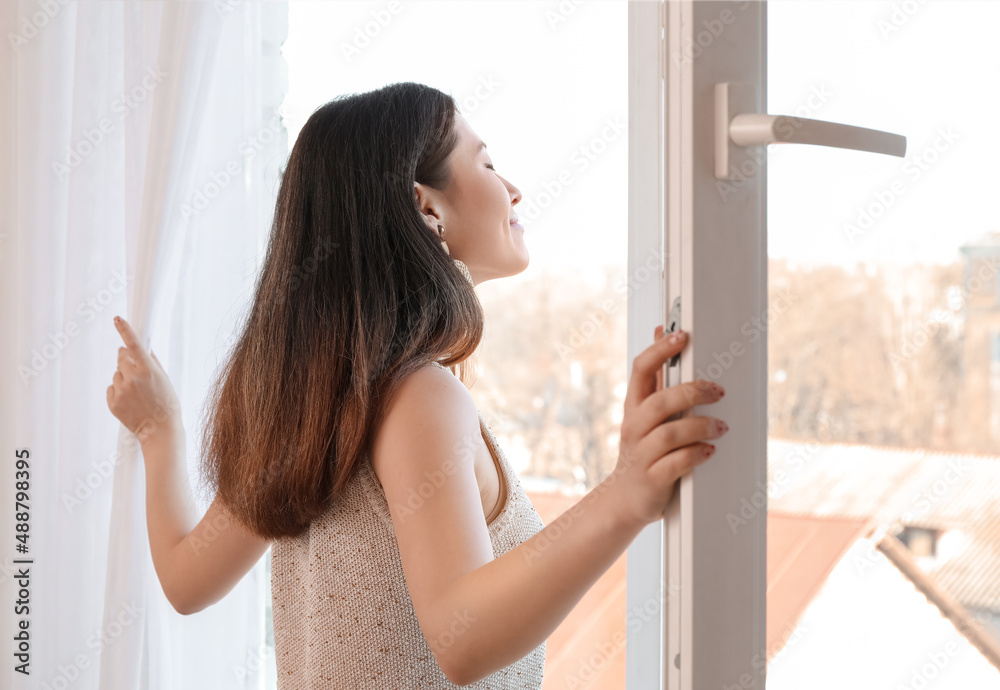 Pretty young Asian woman opening window at home