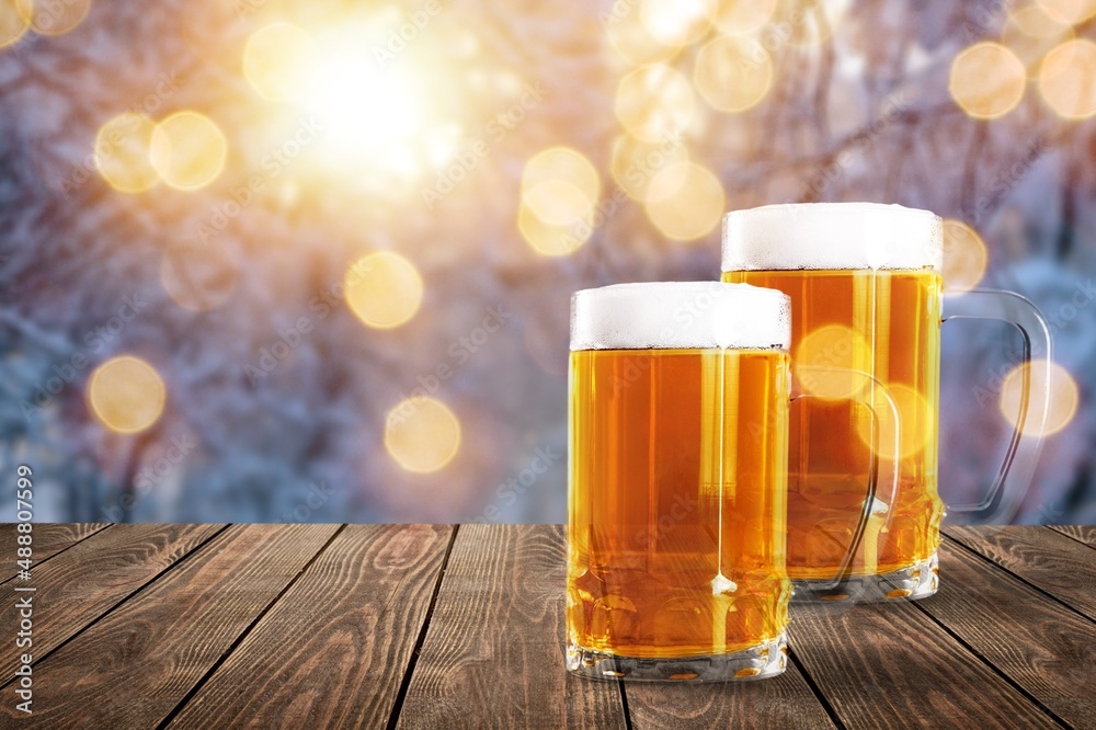 Glass mugs of cold beer with foam served on wooden table at night