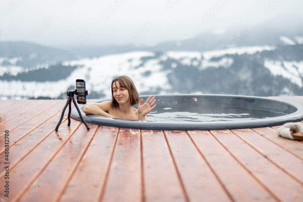 Woman blogging herself on phone while swimming in hot vat at mountains. Concept of influencers and r