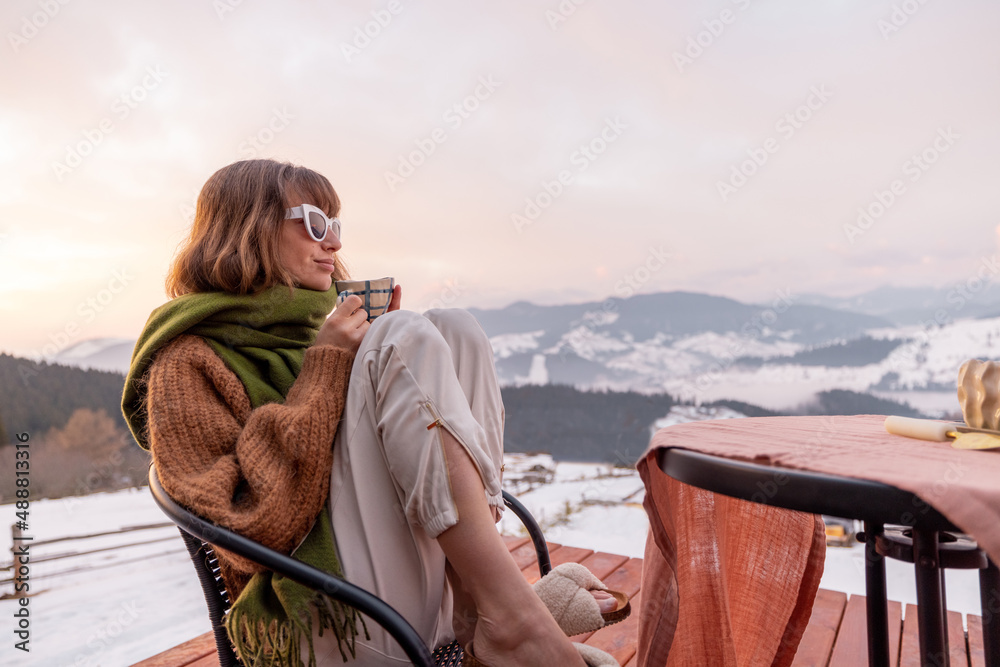 Woman sitting on terrace with great view on the mountains in winter, enjoying drink and beautiful la