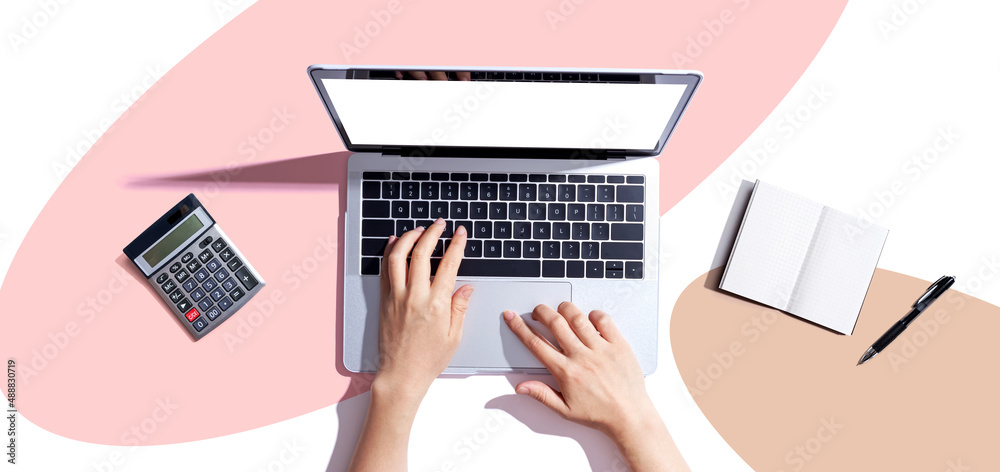 Person using a laptop computer with a notebook and a calculator - flat lay