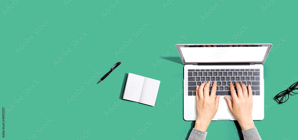 Person using a laptop computer with a notebook and eyeglasses - Flat lay