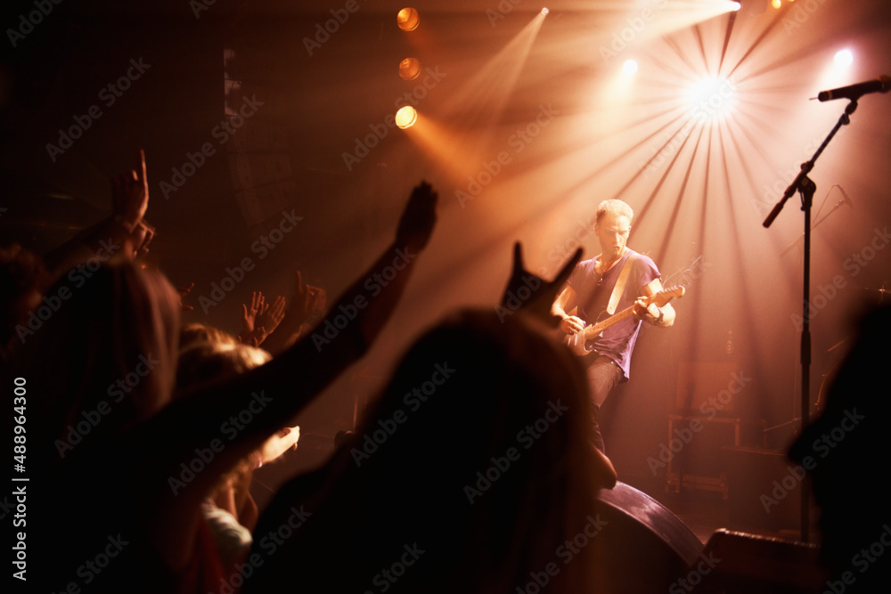 Rear view of an excited crowd cheering their favourite band on beneath the strobe lights at a festiv