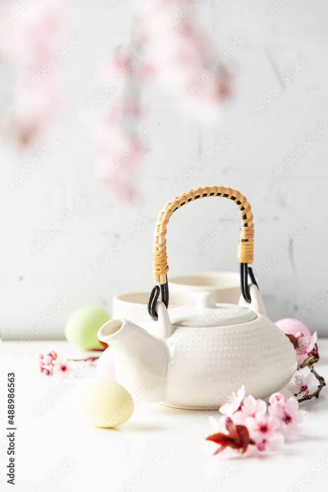 Easter composition with White ceramic teapot, Easter eggs and spring flowers on white table, selecti