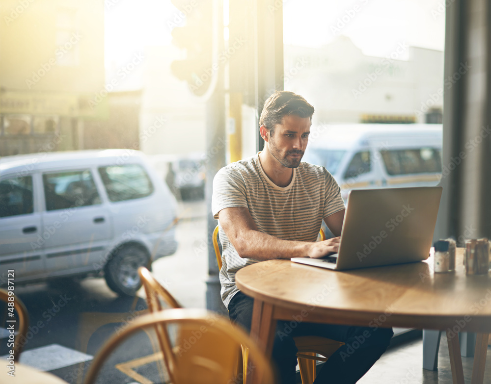 Todays tech allows you to work anywhere. Shot of a young man working on his laptop in a coffee shop.