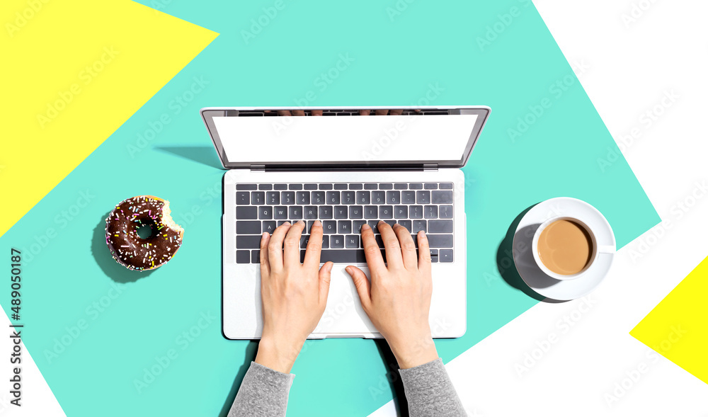 Person using a laptop computer with a donut and a cup of coffee - Flat lay