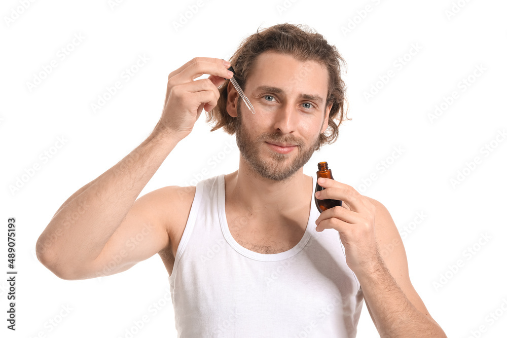 Young man using serum for skin care on white background