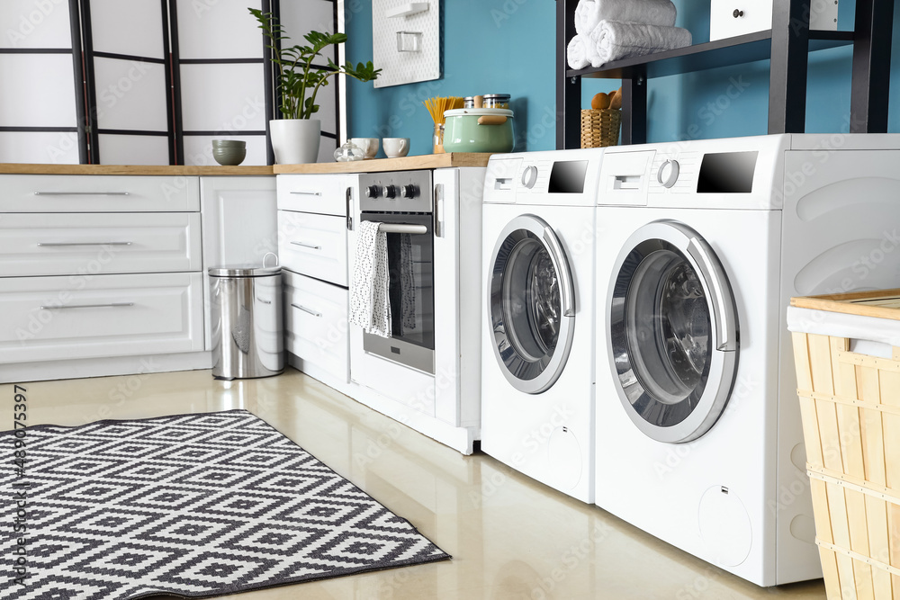 Interior of stylish kitchen with modern washing machines, oven and white counters