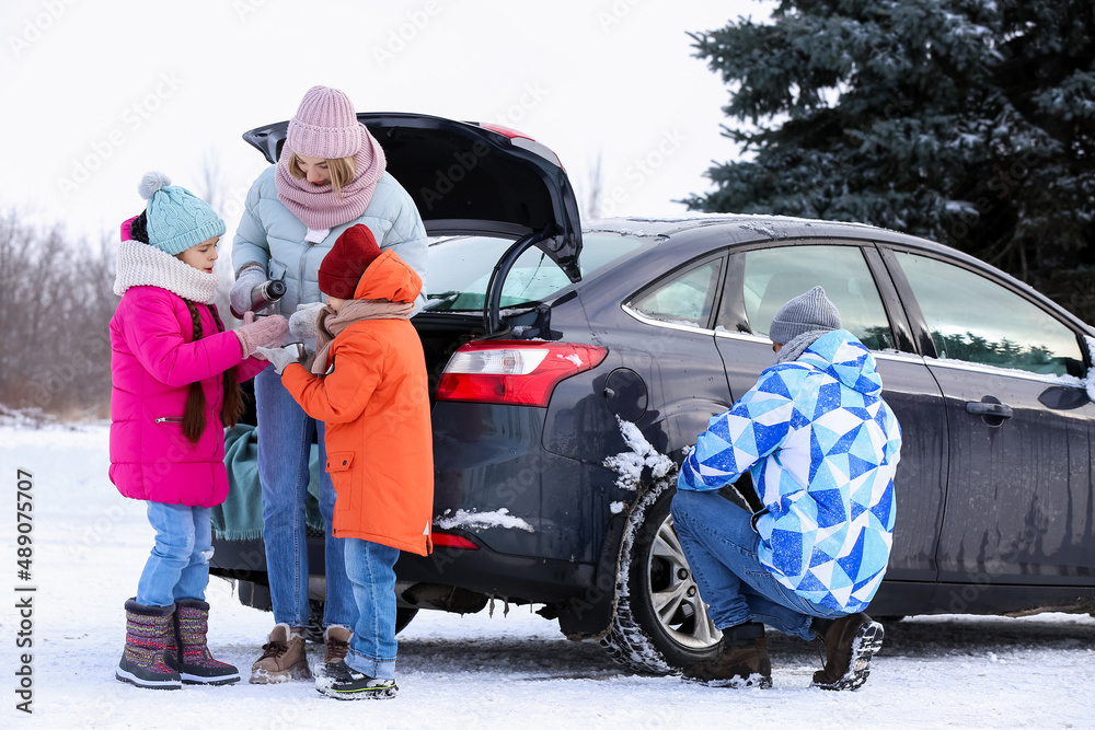 Mother pouring hot tea into her childrens cups on snowy winter day