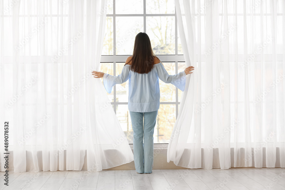 漂亮的年轻女人在房间里拉开窗帘