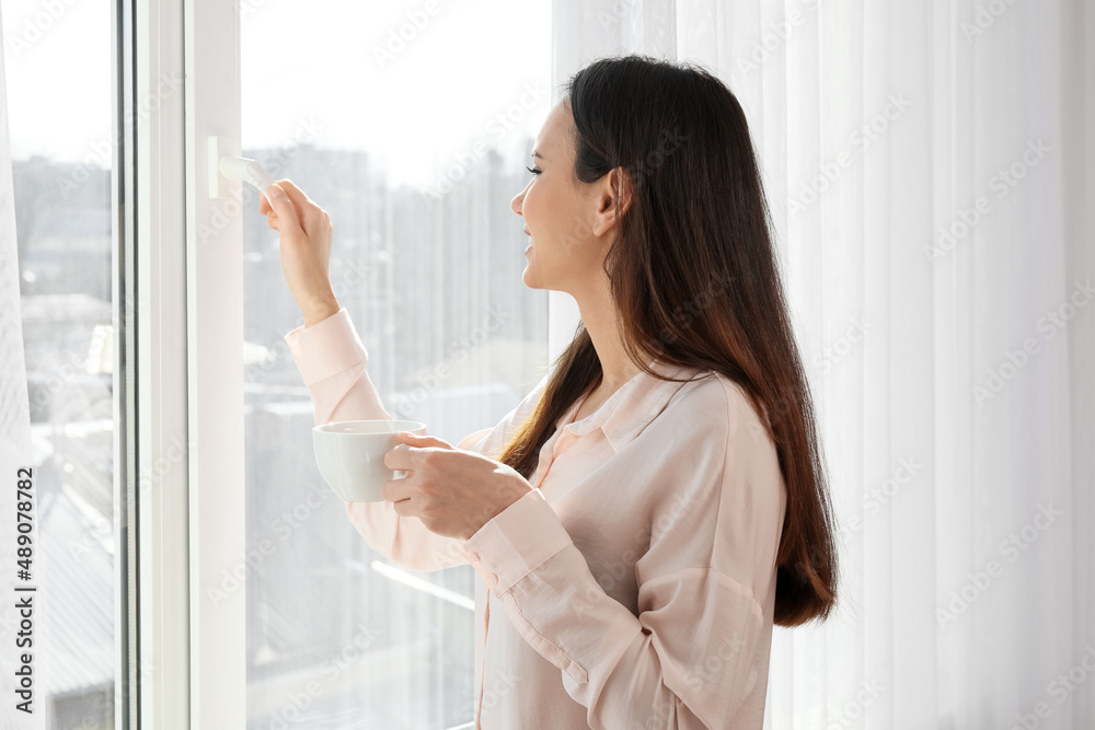 漂亮的年轻女人在窗户附近喝茶