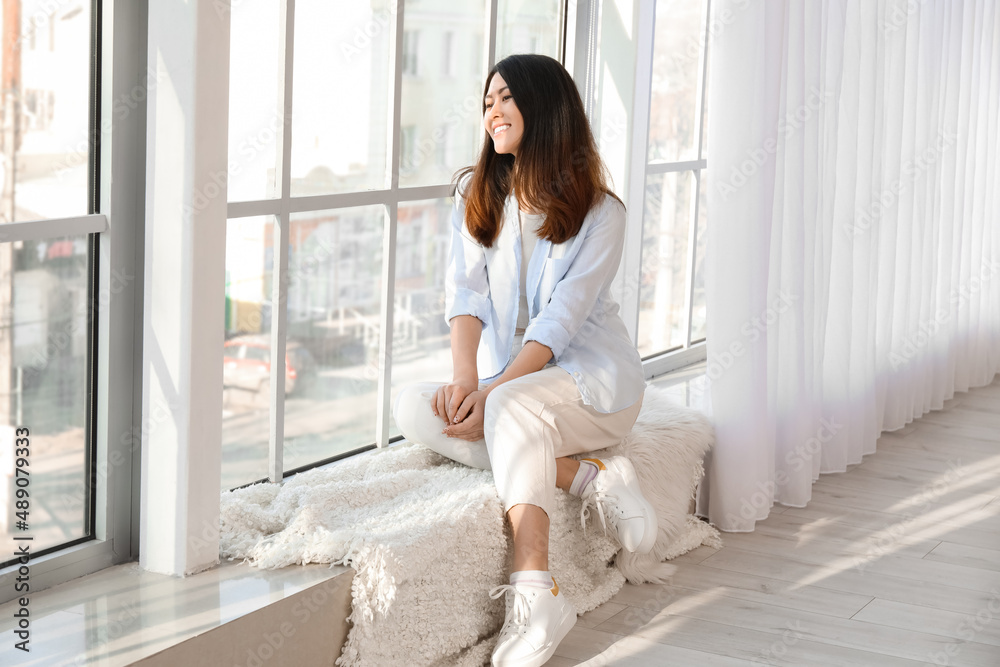 Pretty young Asian woman sitting on window sill