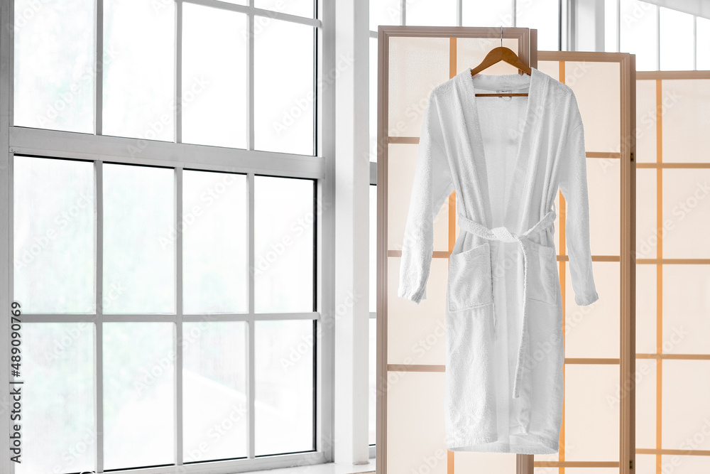 Folding screen with bathrobe near window in light bathroom