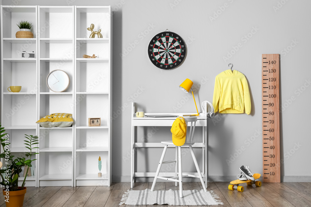 Interior of light childrens room with workplace, shelving unit and dartboard