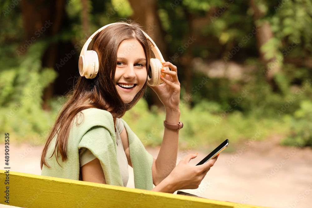 Young female tourist with phone listening to music in green park