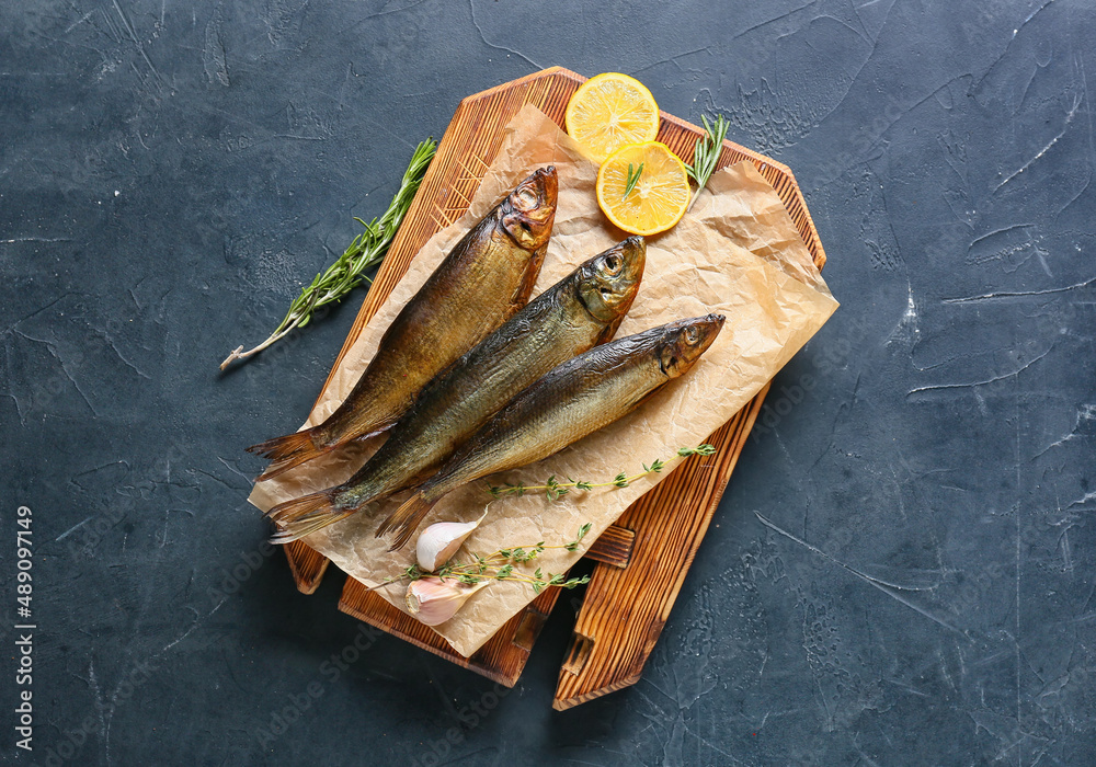 Wooden board with smoked herring fishes on black background