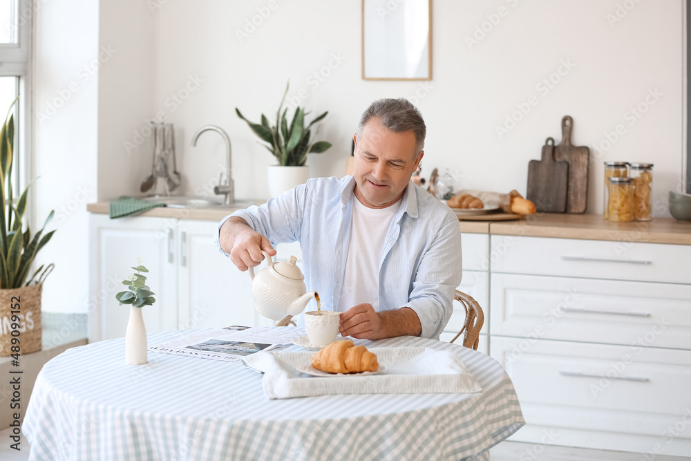 一位老人在厨房的桌子上把茶倒进杯子里