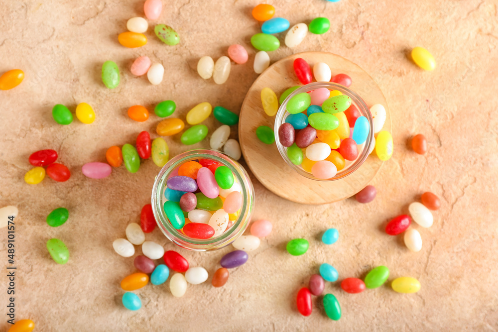 Jar and bowl with different jelly beans on beige background