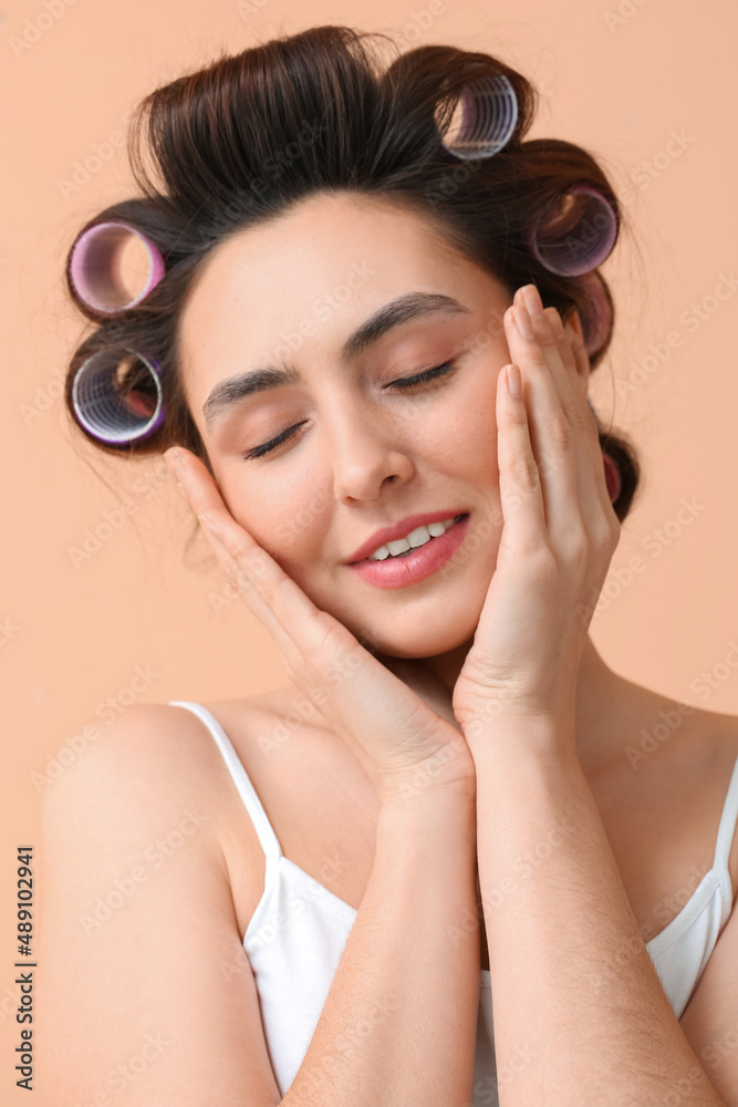 Beautiful young woman in hair rollers on color background