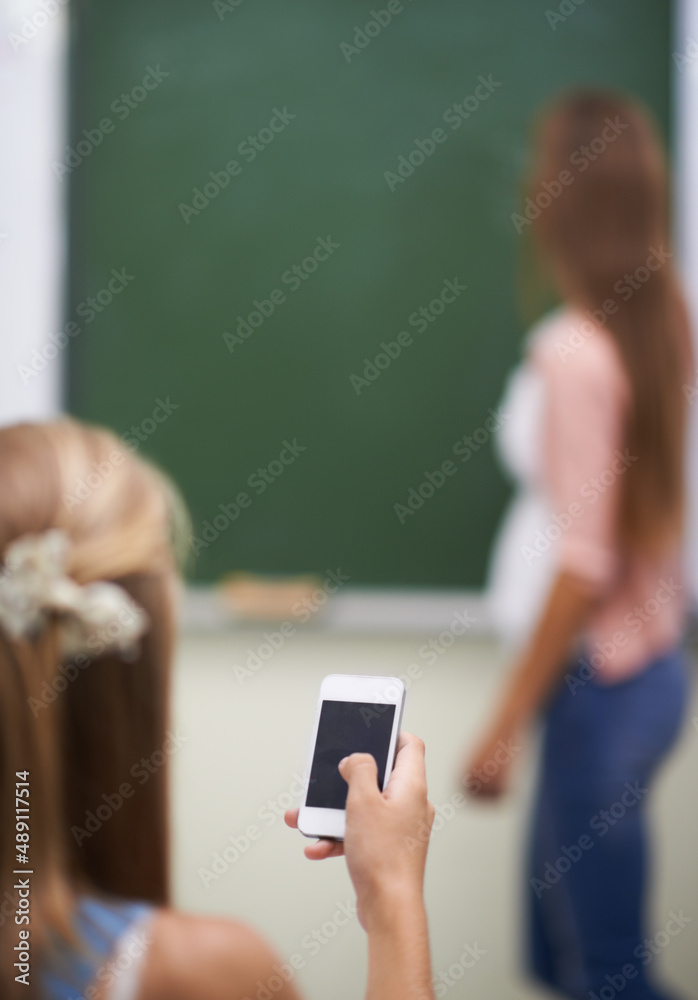 Looking for answers on her mobile. Over the shoulder shot of a young girl using her cellphone in cla