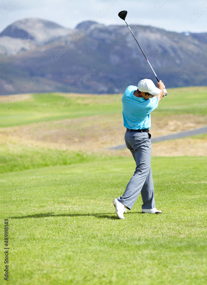 Driving it down the fairway. A young, fit male golfer following through after driving his ball down 