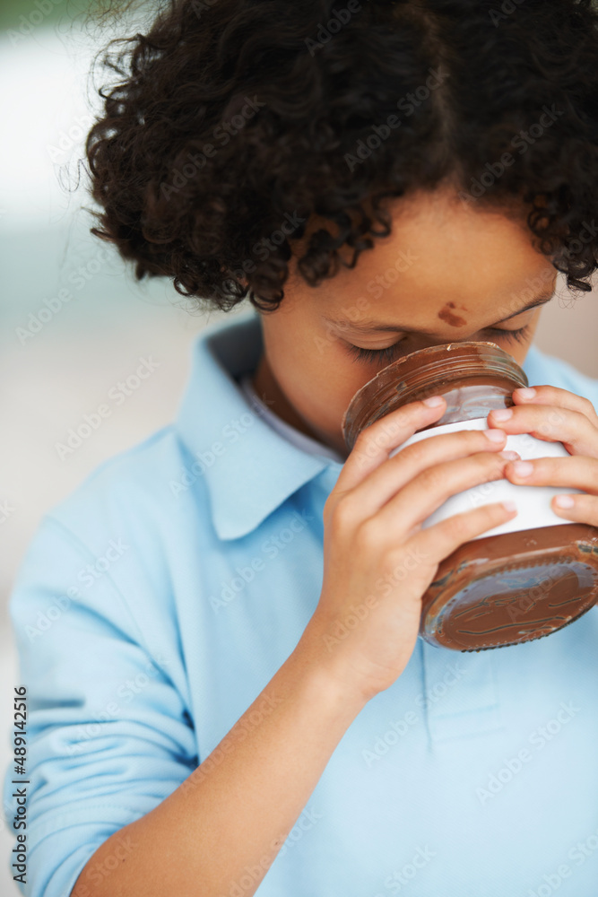 A treat for the tounge. A little boy eating Nutella from a jar.