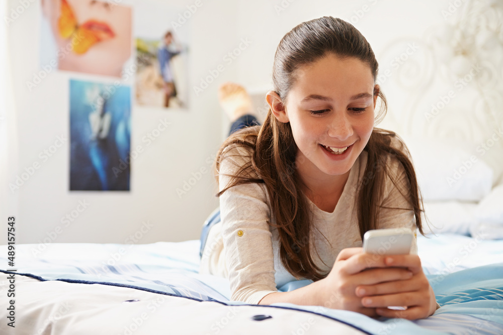 Planning something big. Shot of a teenage girl lying on her bed and texting on her phone.