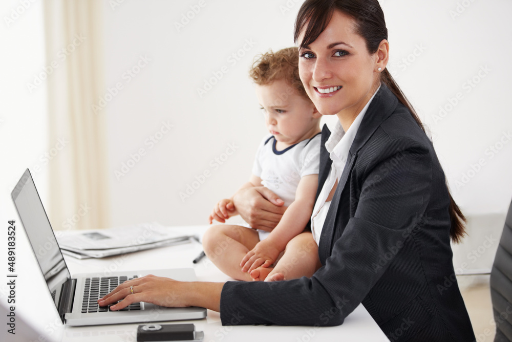 Managing career and motherhood with ease. Young working mom smiling at the camera while holding a ca