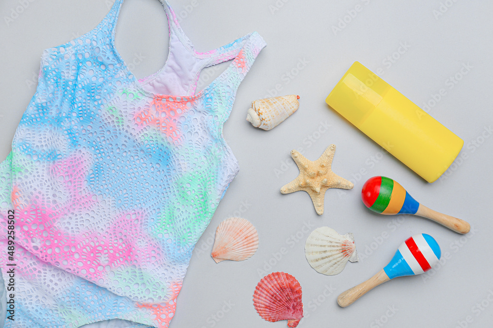 Composition with stylish swimsuit, bottle of sunscreen, seashells and maracas on white background