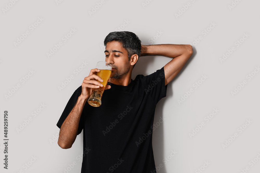 Handsome man drinking beer on light background