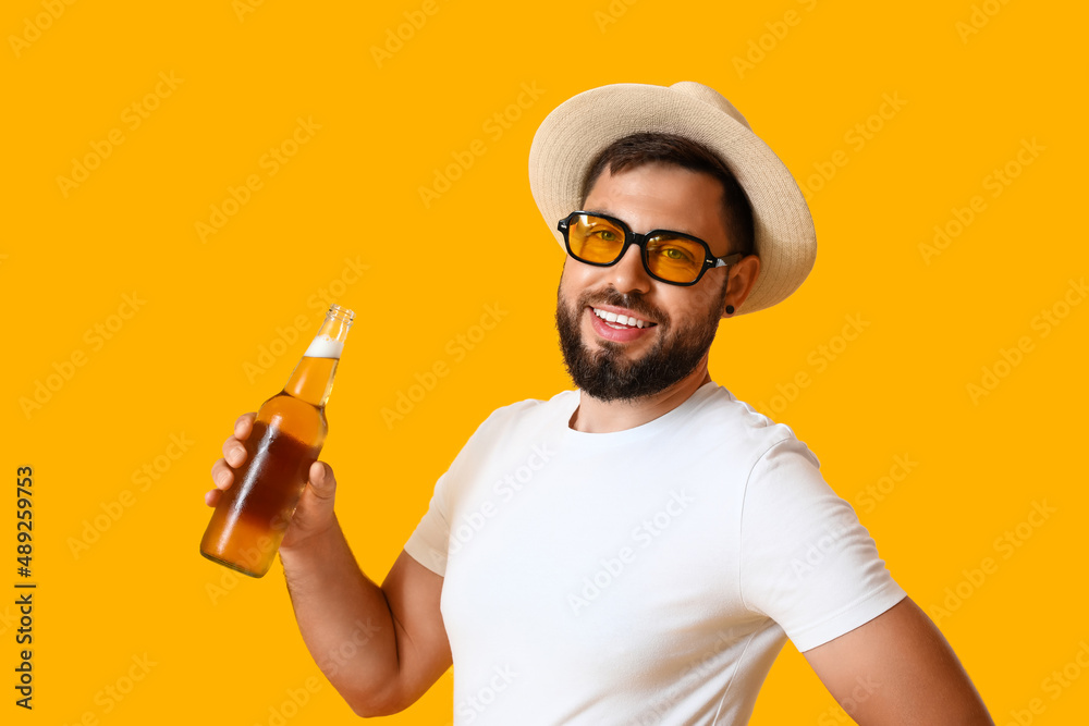 Young man in sunglasses with bottle of beer on yellow background