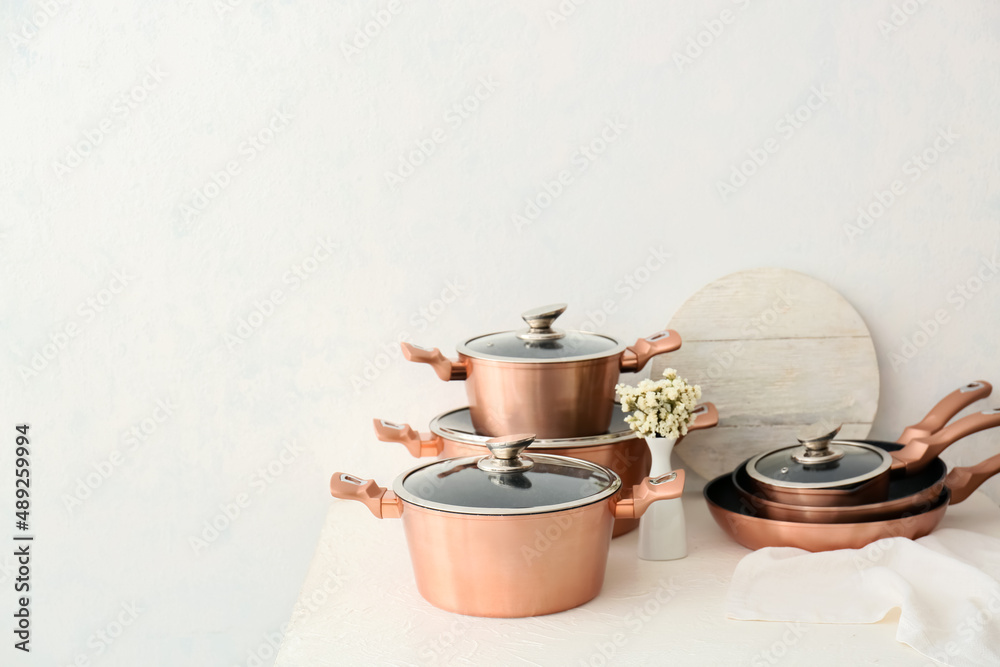 Set of copper kitchen utensils and vase with flowers on table against white background