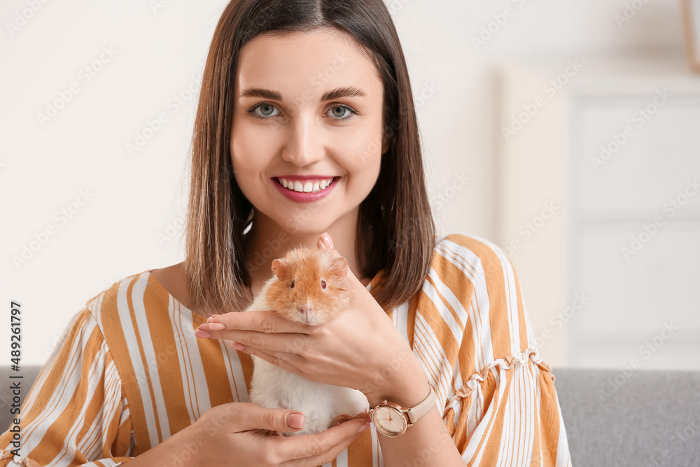 Beautiful young woman with cute guinea pig at home