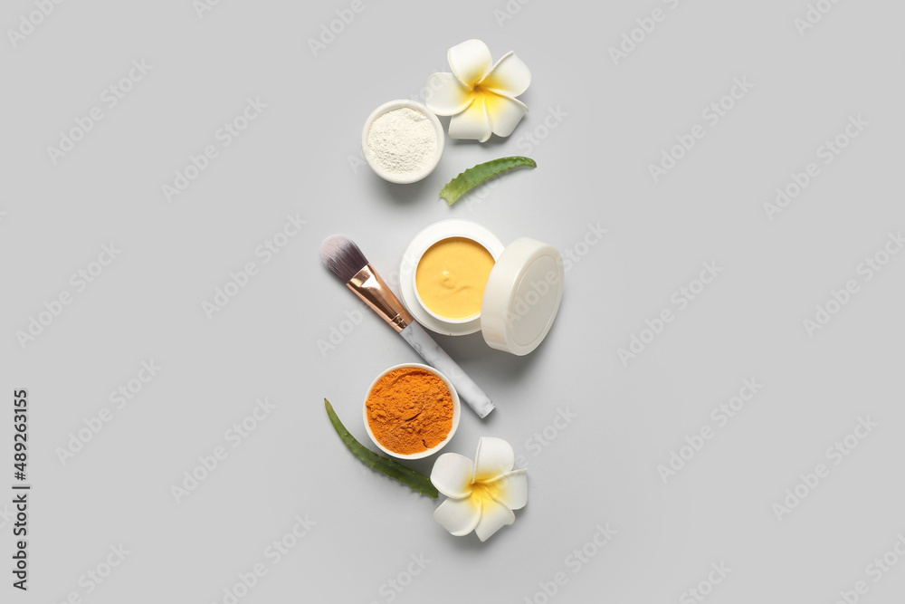 Composition with turmeric mask, powder, makeup brush and flowers on light background