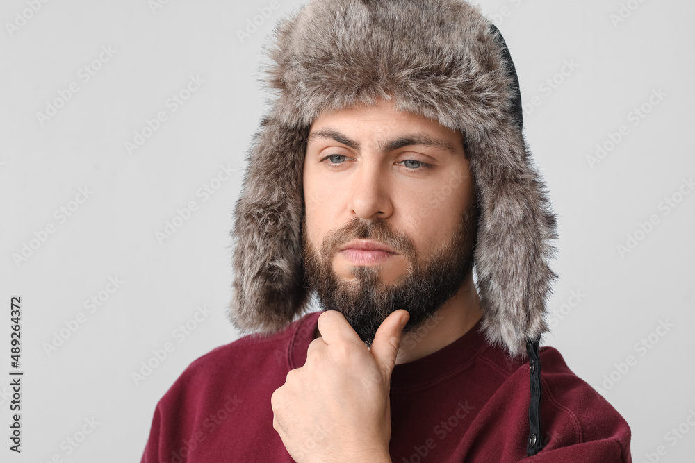 Stylish bearded man in sweater and ear-flapped hat on light background