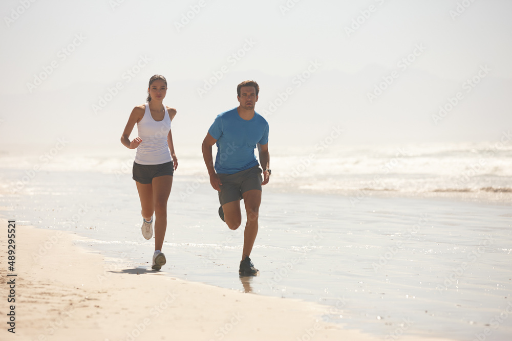 Challenge accepted. Shot of a young couple jogging together on the beach.