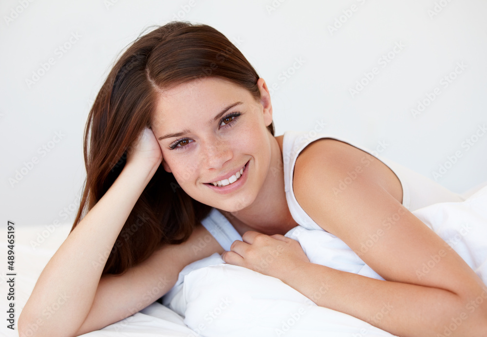 Enjoying sleeping in while on holiday. A gorgeous young woman smiling while lying in bed.