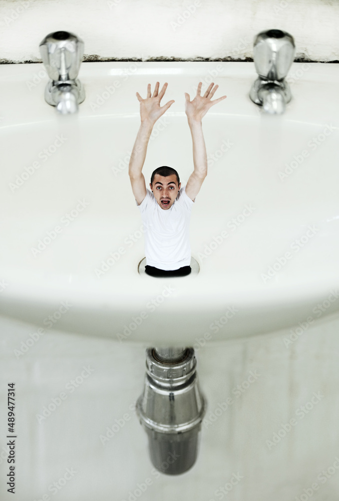 Feeling drained. A young man being sucked down the drain in a giant basin.