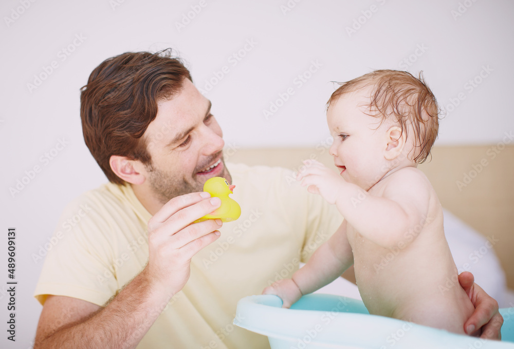 I want to play with that. A young father showing his baby girl a toy while shes in the bathtub.