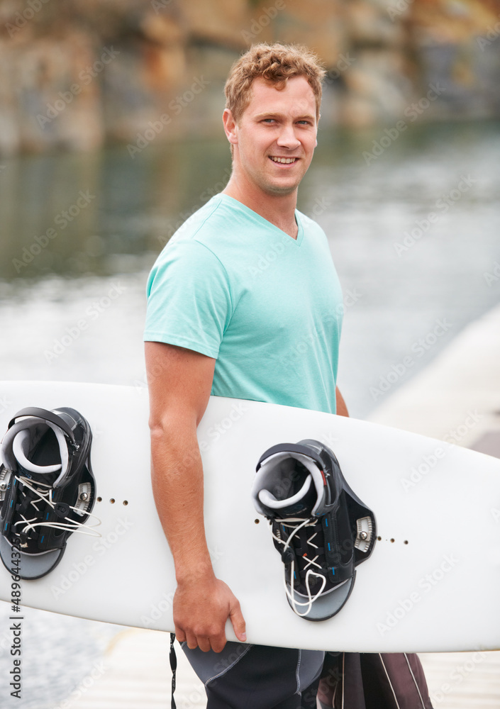 Hes an avid wakeboarder. Smiling wakeboarder holding his wakeboard alongside the lake.