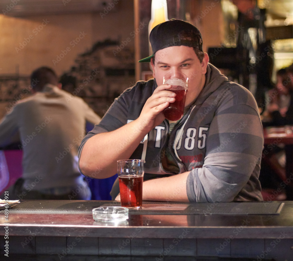 He enjoys a cold beer every Friday after work. Portrait of a young man drinking at the local bar.